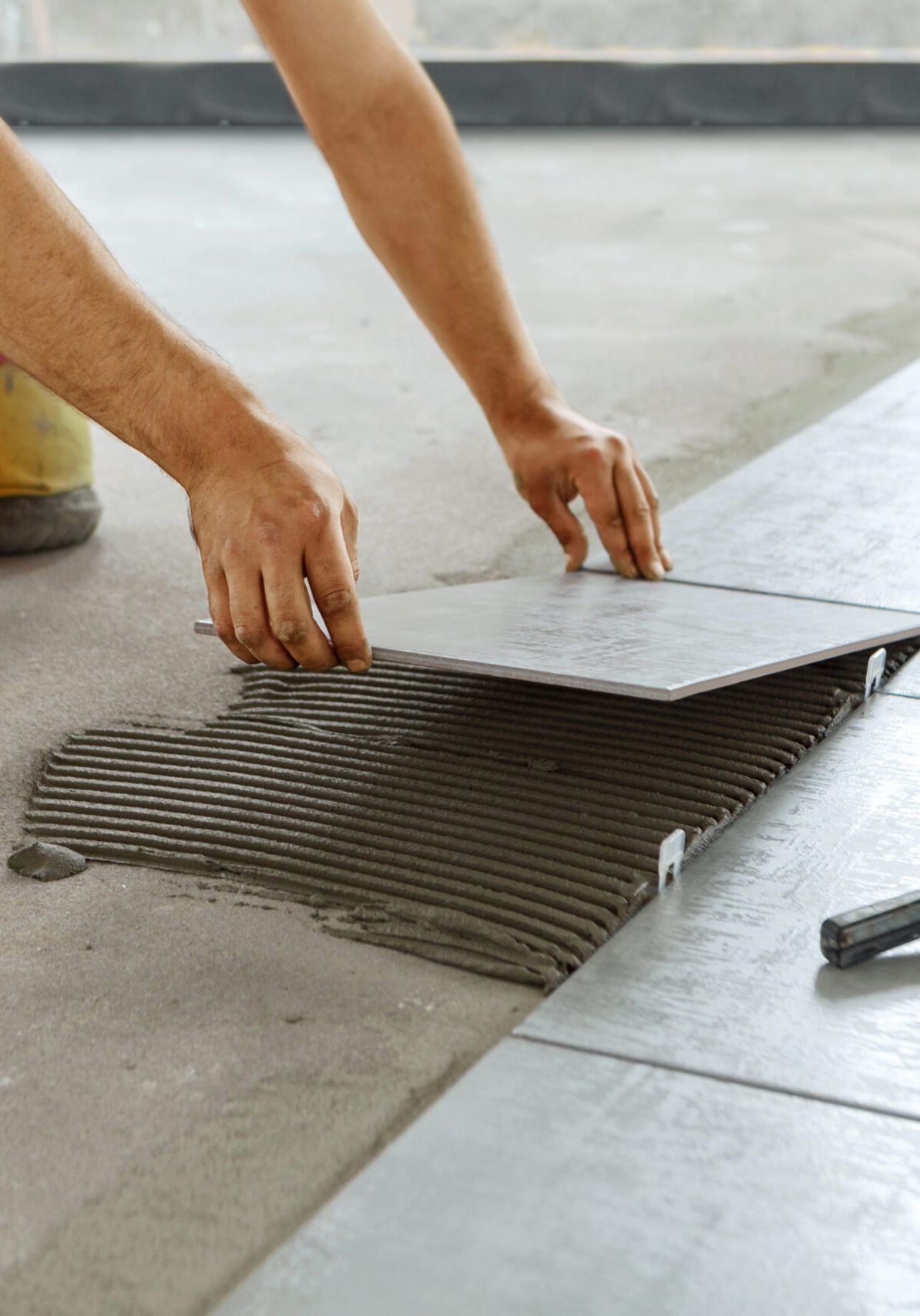 Ceramic Tiles. Tiler placing ceramic wall tile in position over adhesive with lash tile leveling system - Image